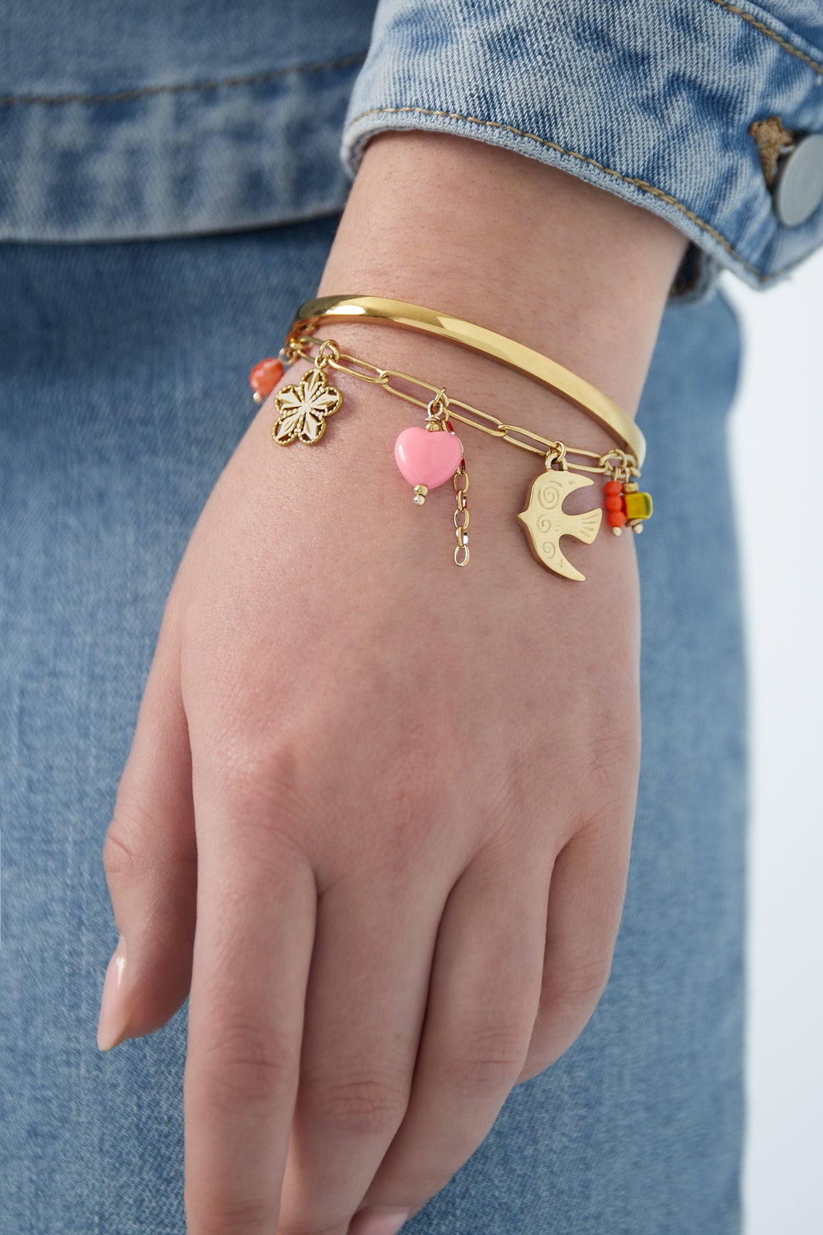 Close-up of golden charm bracelet worn with a blue denim jacket sleeve