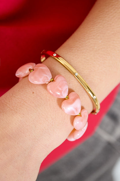 Pink heart-shaped bead bracelet on wrist with gold bangle, red sweater background