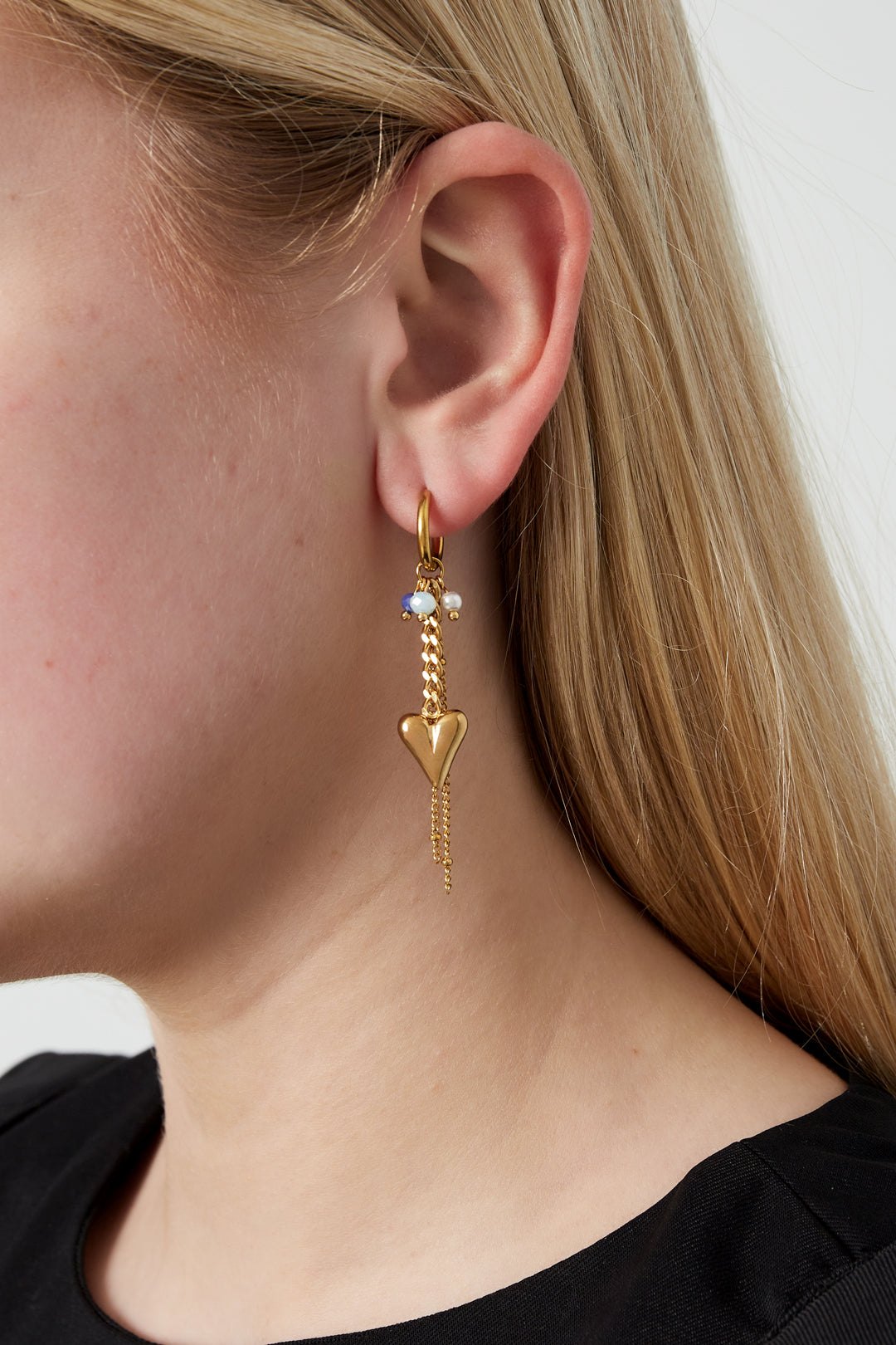 Side profile of a model wearing gold-tone heart drop earring with pearl and blue beads