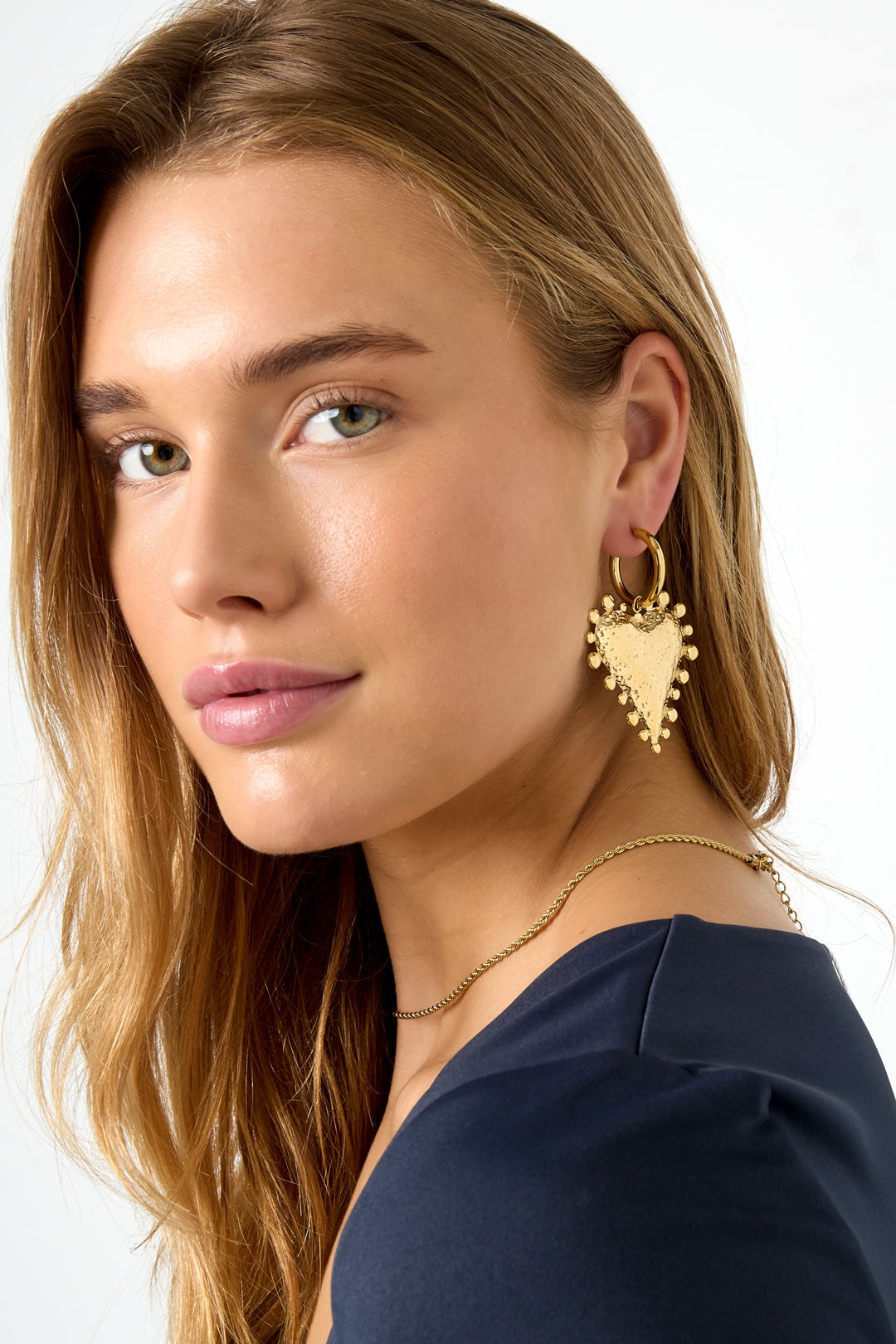 Model wearing gold textured heart hoop earrings with natural makeup and a navy top
