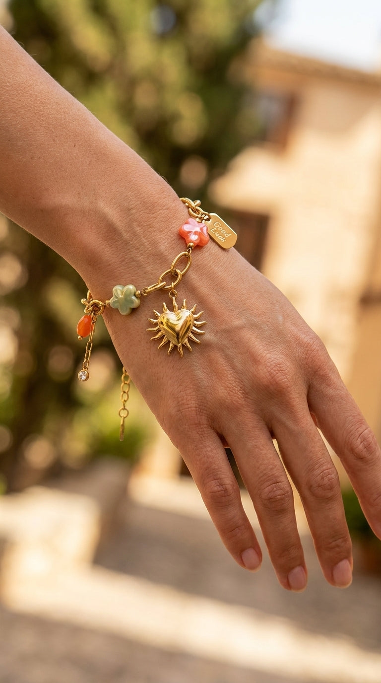 Charm Era Unlocked gold-tone link bracelet with sun-heart, colorful flower charms, and Good Luck tag on a wrist.