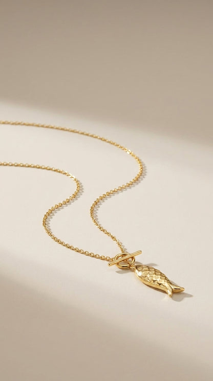Gold Catching Vibes necklace featuring a textured fish pendant and a delicate toggle clasp on a thin chain.