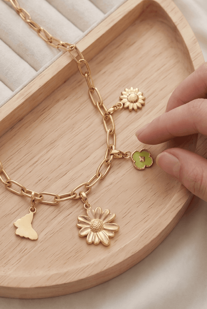 Gold-tone chain bracelet featuring dainty floral, butterfly, and green clover charms on a wooden tray.