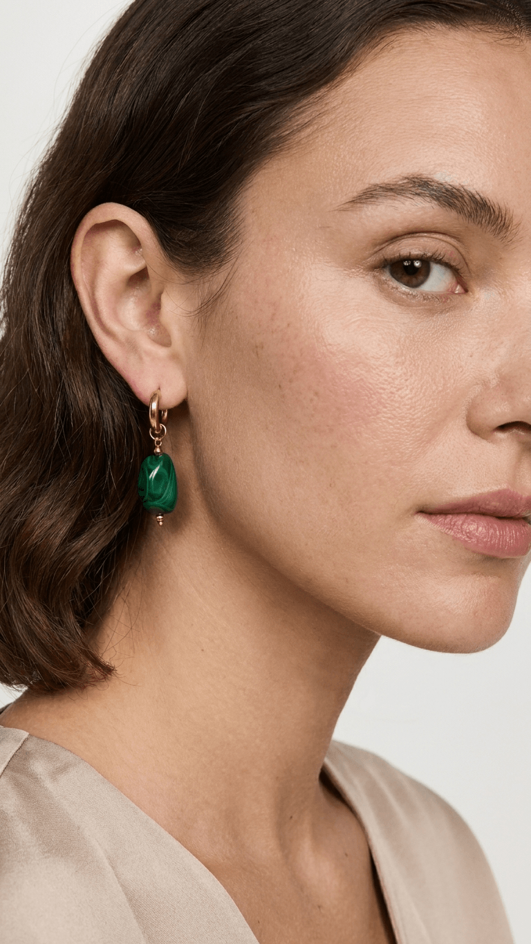 A gold hoop earring featuring a smooth, vibrant green malachite pebble charm. Minimalist, modern style.