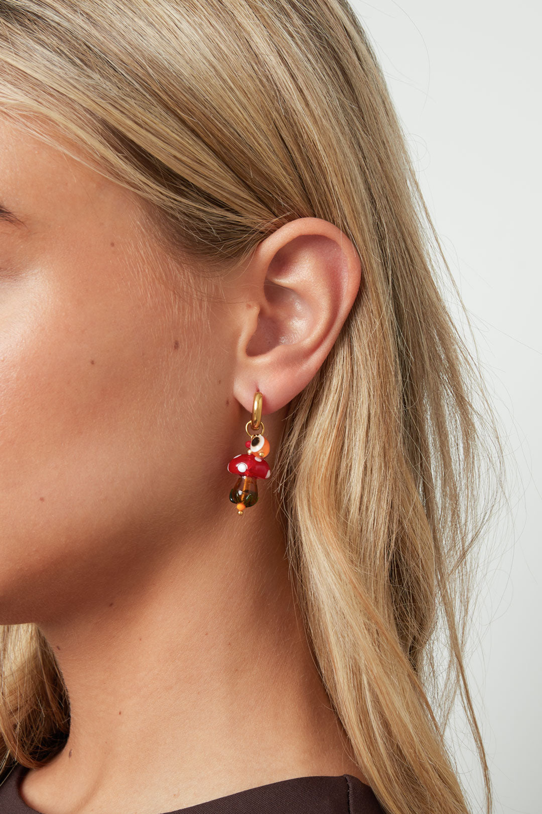 Close-up of a woman wearing one whimsical mushroom hoop earring with red and white glass mushroom charm