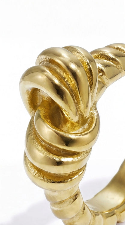 Close-up of a polished gold Ribbon Knot ring with a textured, intricate knotted design on a white background.