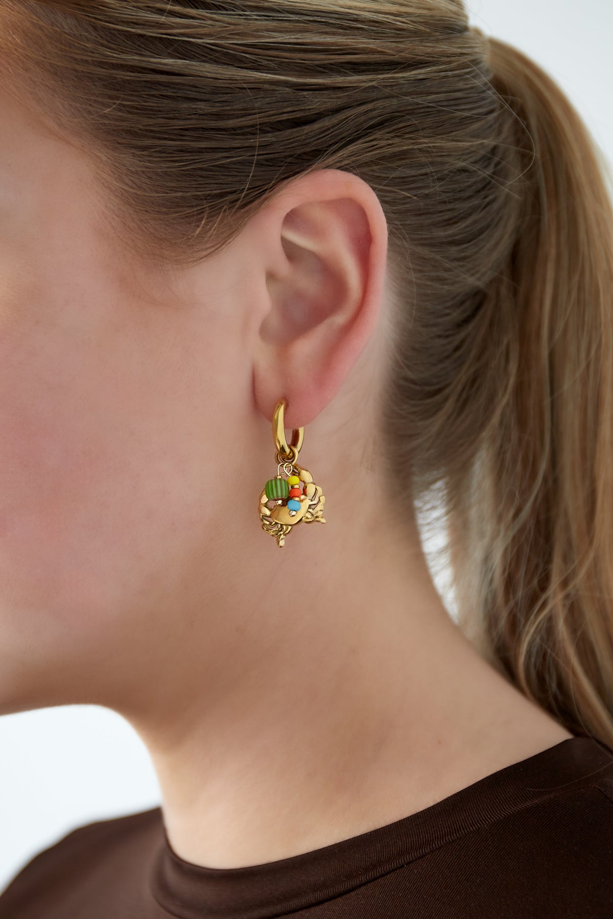 Close-up view of a woman wearing gold crab charm earring with green, yellow, orange, and blue beads