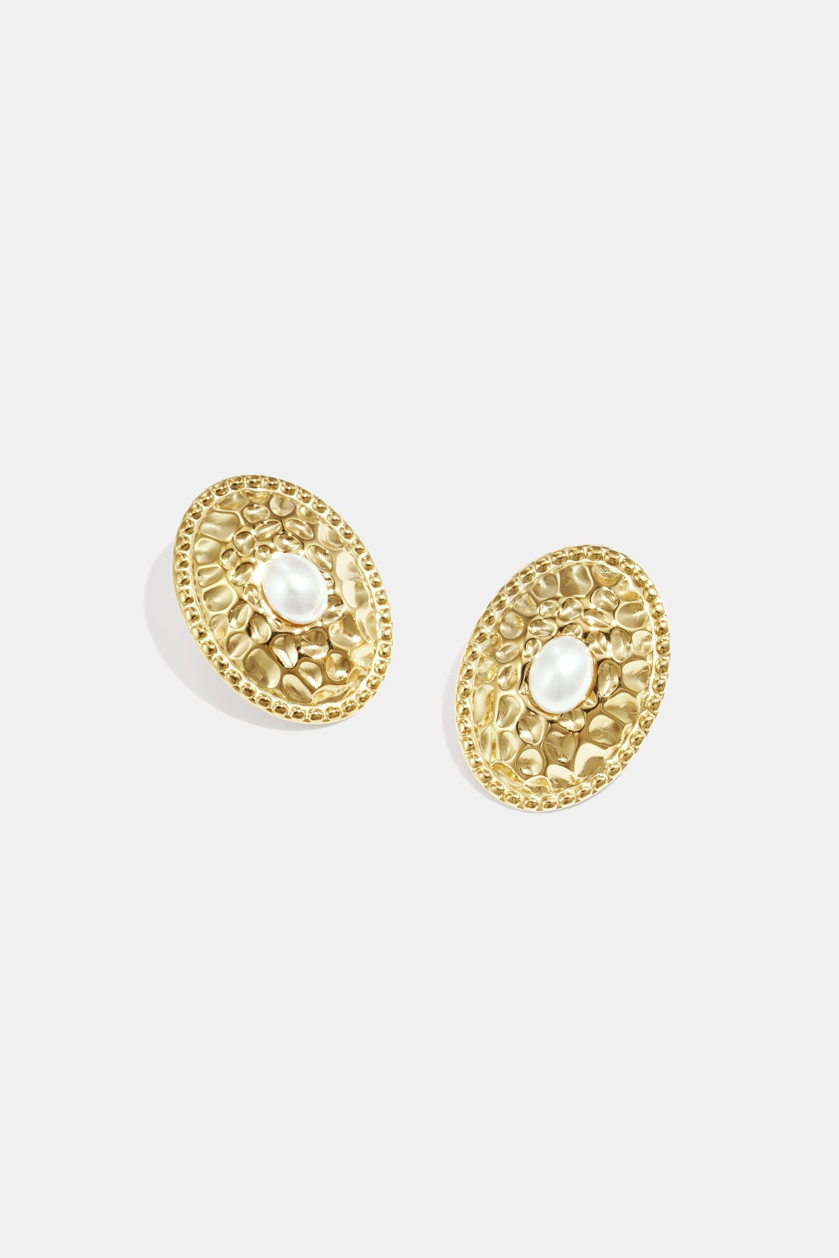 Close-up of gold-tone oval stud earrings with hammered texture and pearl center on white background