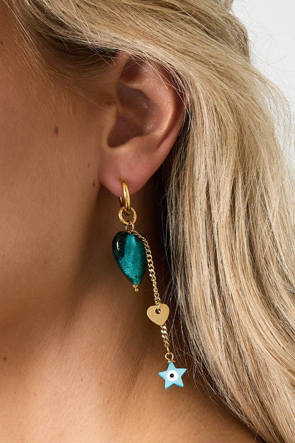 Close-up side profile of a woman wearing the gold-tone drop earring featuring emerald-green heart and dangling gold heart and blue star charms