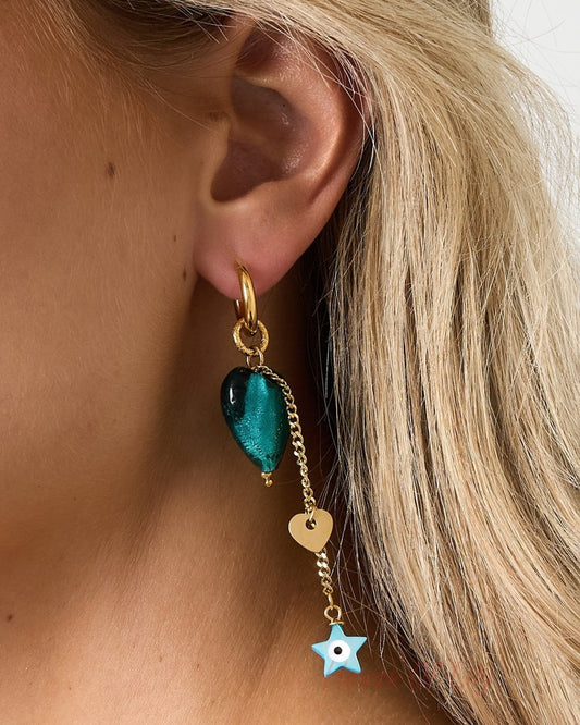 Close-up side profile of a woman wearing the gold-tone drop earring featuring emerald-green heart and dangling gold heart and blue star charms