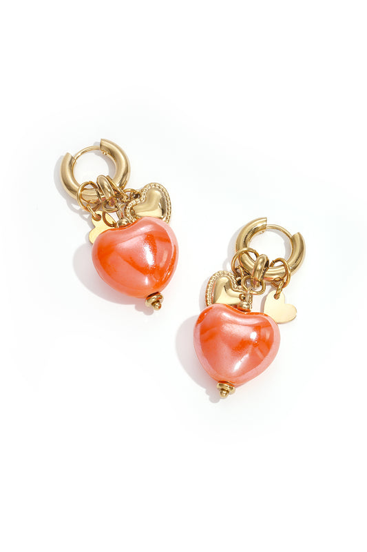 Pair of gold hoop earrings with bright orange glossy heart charms and smaller gold heart pendants on a white background