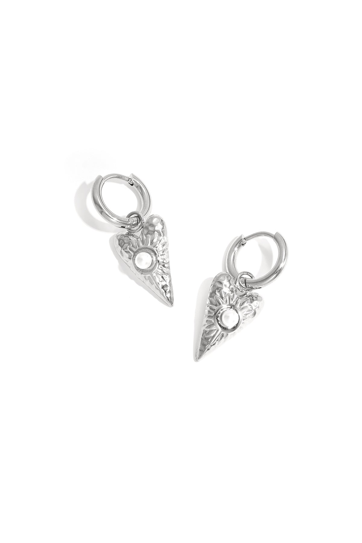 Close-up of silver heart-shaped drop earrings with pearl detail on white background