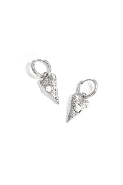 Close-up of silver heart-shaped drop earrings with pearl detail on white background