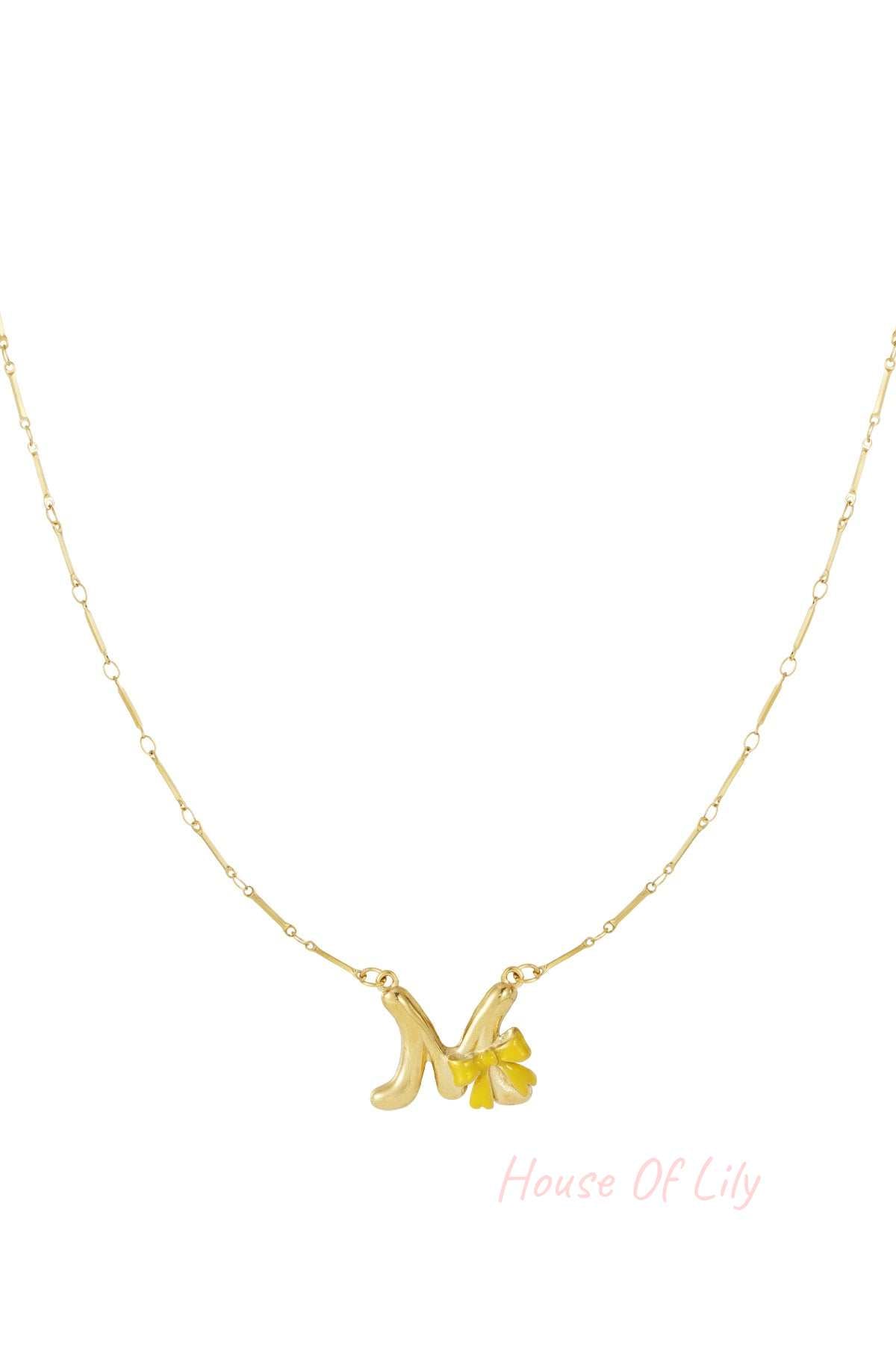 Gold chain necklace with a letter M pendant accented by a small, bright yellow enamel bow charm.