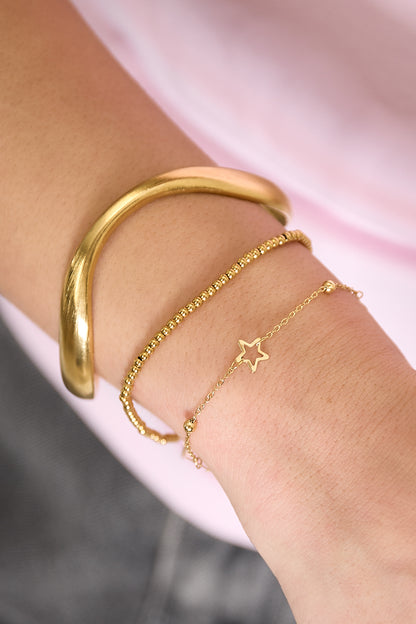 Woman’s wrist with layered bracelets: a gold organic sculpted cuff, a gold bead bracelet, and a delicate chain bracelet with a star charm