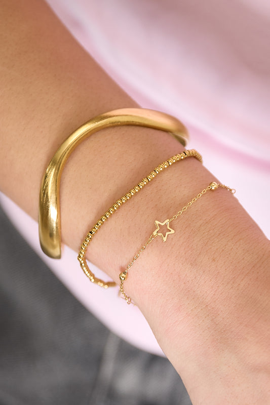 Woman’s wrist with layered bracelets: a gold organic sculpted cuff, a gold bead bracelet, and a delicate chain bracelet with a star charm