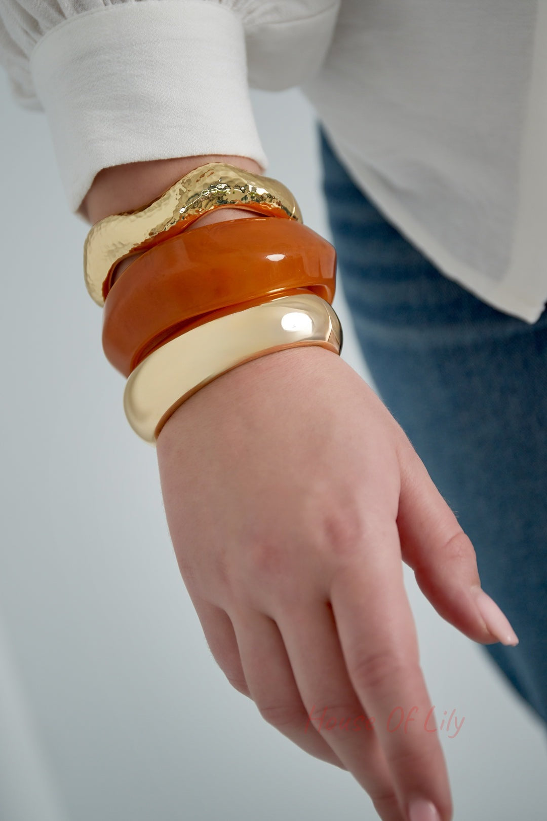 Woman wearing stacked chunky bracelets including a smooth gold bangle, amber resin bangle, and hammered gold bangle with a casual outfit