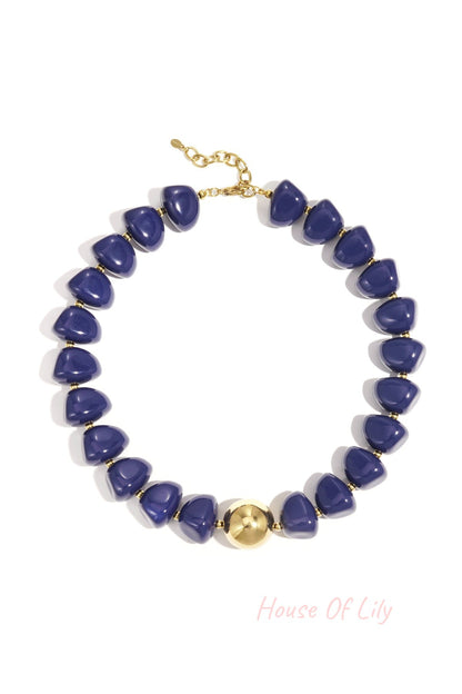 Close-up of a chunky blue beaded necklace with gold accent bead and clasp on white background