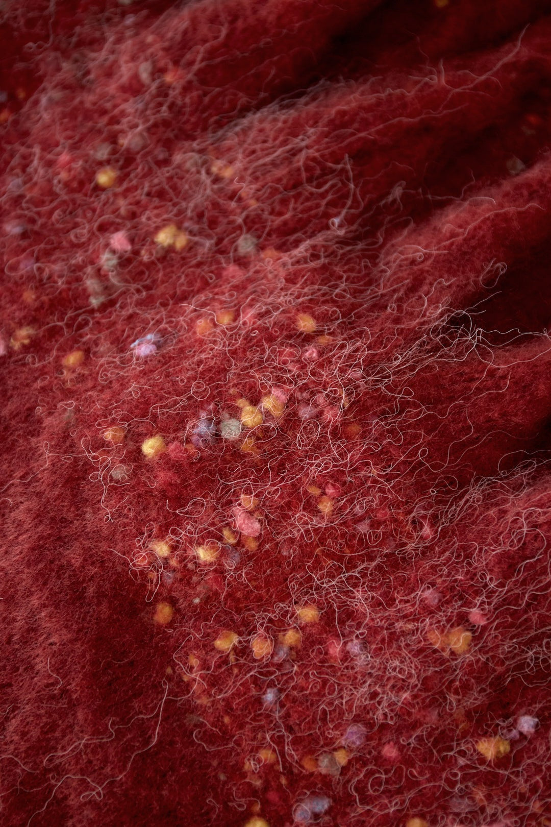 Close-up macro shot of brick red fabric showing fluffy yarn and colorful confetti details