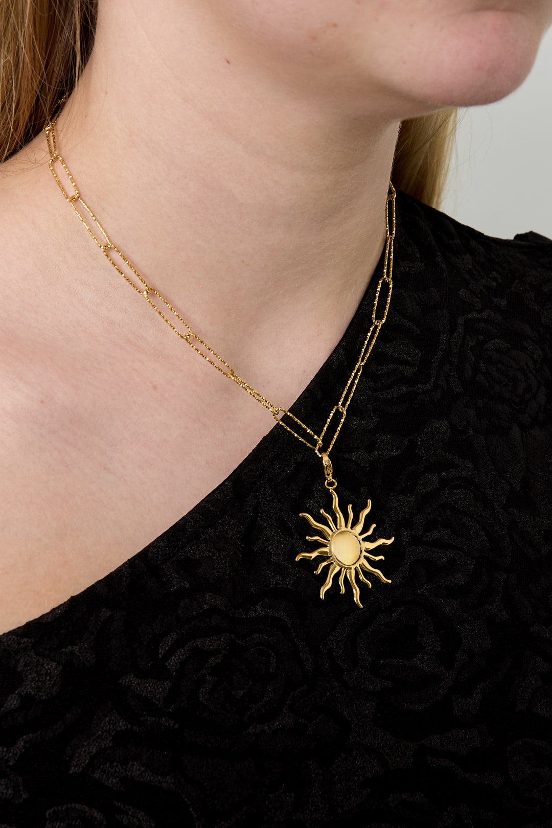 Woman wearing gold paperclip chain necklace with sun-shaped pendant on black top