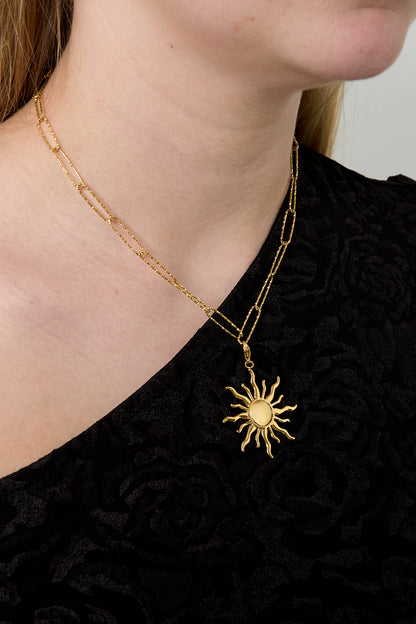 Woman wearing gold paperclip chain necklace with sun-shaped pendant on black top