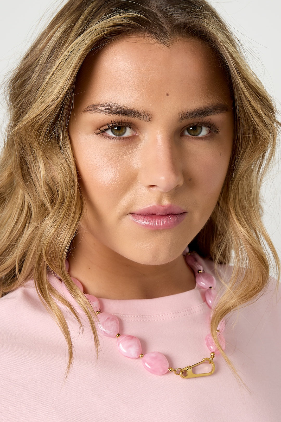 Model wearing pastel pink chunky resin beaded necklace with gold-tone front clasp, paired with a soft pink top