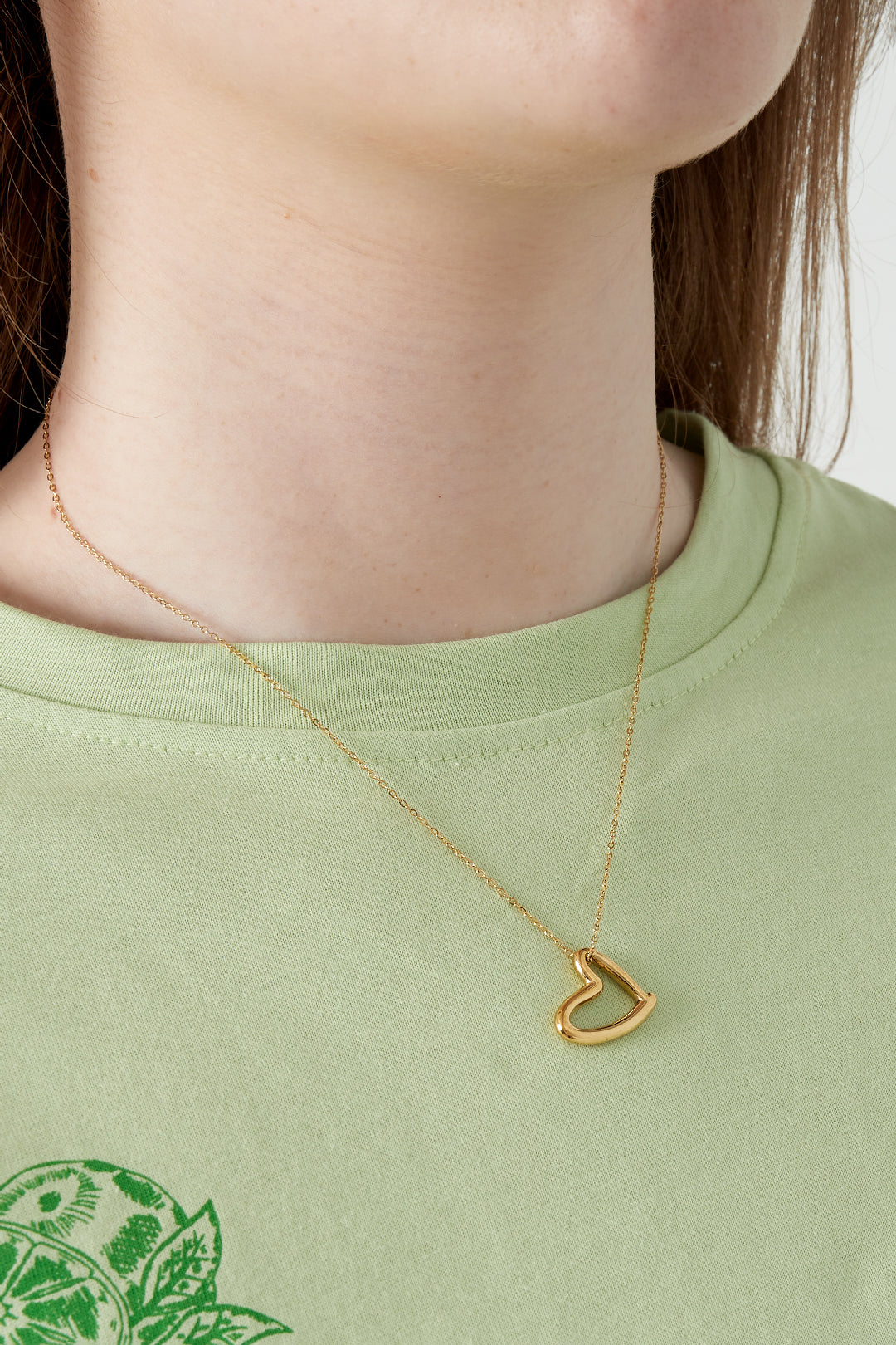 Close-up of woman wearing the gold heart pendant necklace with a light green top