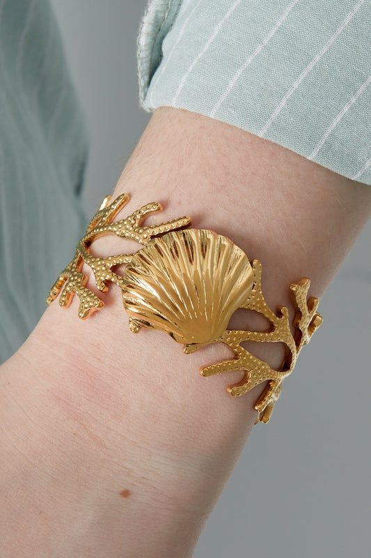 Close-up of golden seashell cuff bracelet worn on wrist with striped light blue shirt