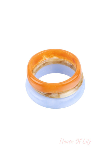 Three resin bangles stacked: orange marbled, beige marbled, and light blue, on white background