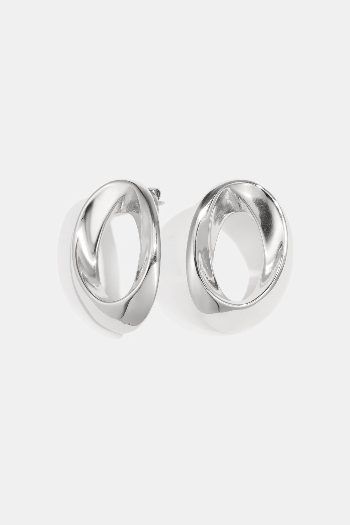 Pair of polished silver-tone twisted oval hoop earrings on white background