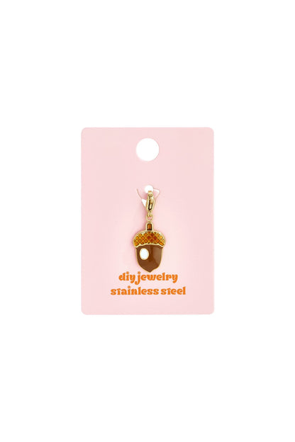 Cute Acorn Drop charm made of gold-tone stainless steel with brown and orange enamel details on a pink display card.