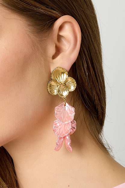 Side profile of woman wearing gold flower drop earrings with pink textured petals, highlighting shine and detail