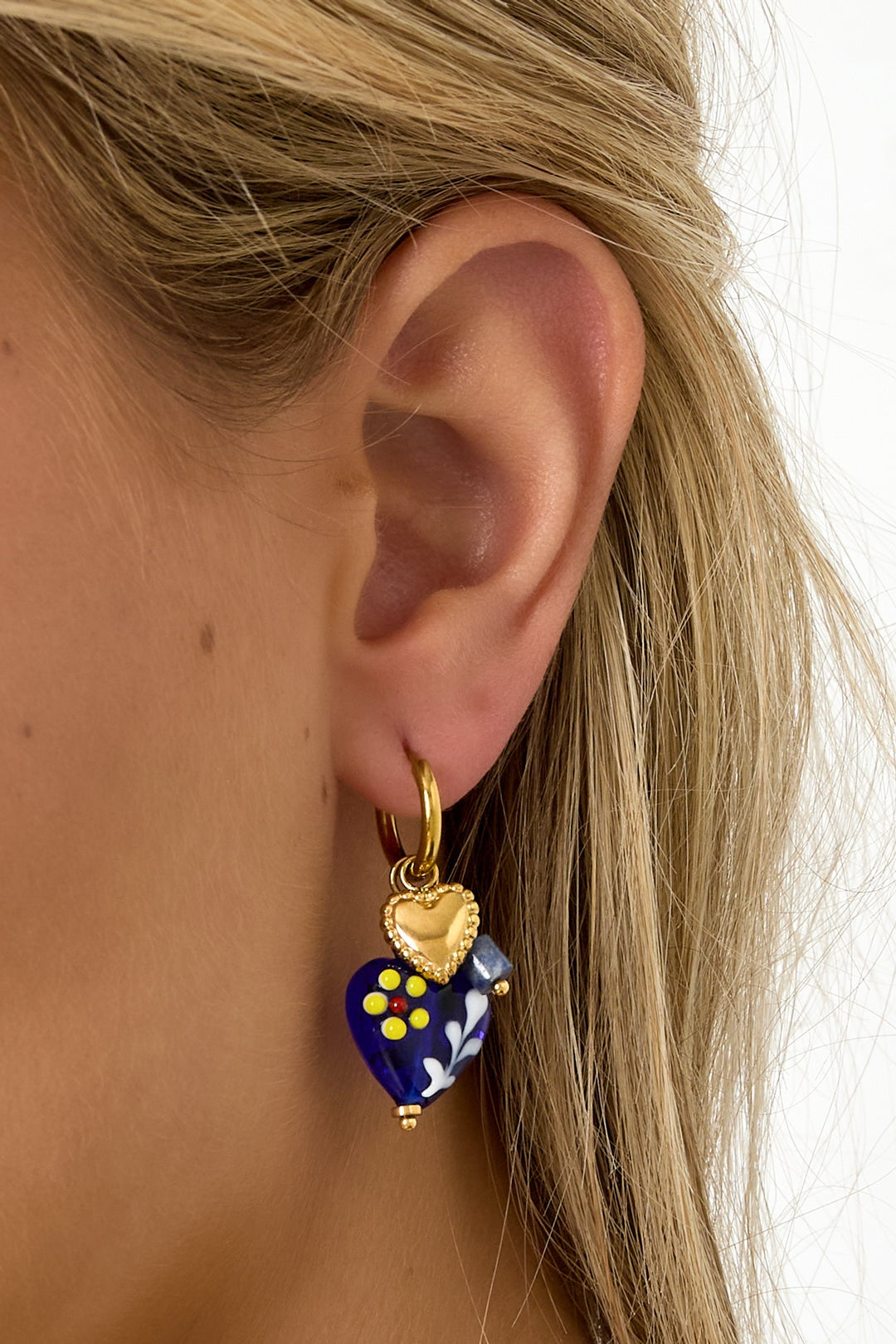 Woman wearing gold heart hoop earrings with blue floral heart charms viewed from the side