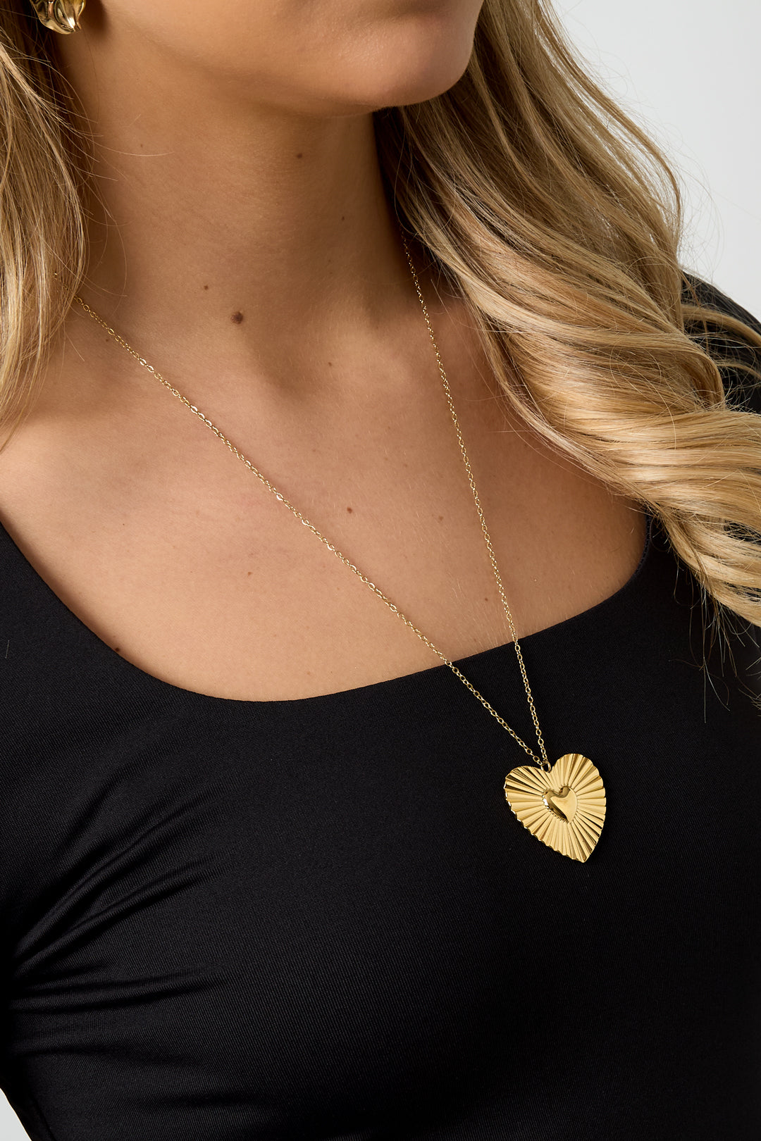 Model wearing the gold heart pendant necklace against black top highlighting youthful and minimal aesthetic