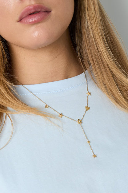Gold lariat necklace featuring small star and heart charms worn by a woman against a light blue top.