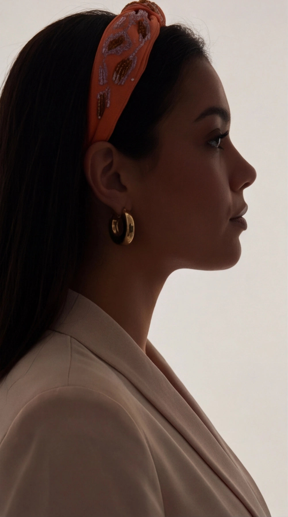 A side profile of a woman wearing polished gold hoop earrings, round and chunky in style.