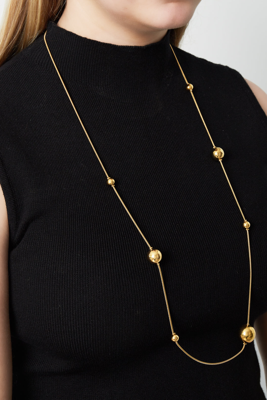 Woman wearing the elegant long gold bead necklace over a sleeveless black top