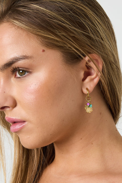 Close-up side profile of woman wearing gold floral hoop earrings with colorful beads