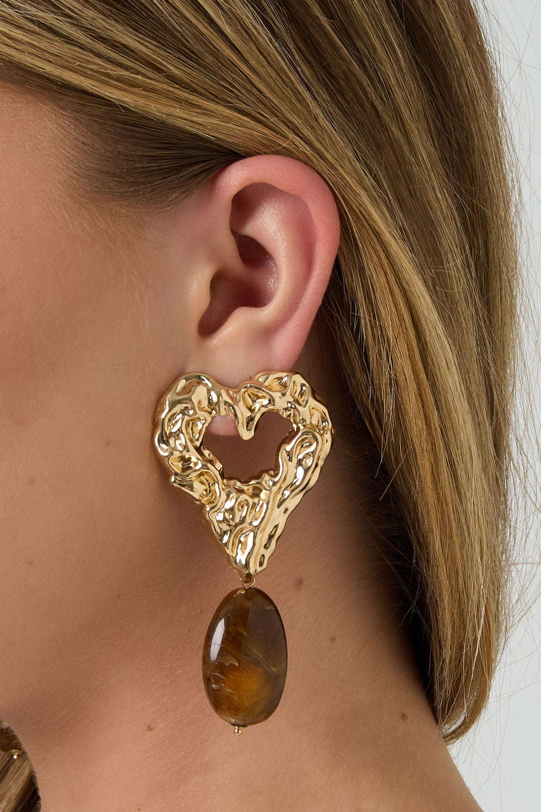 Close-up of gold-tone textured heart earring with brown marbled resin drop worn by a woman with blonde hair