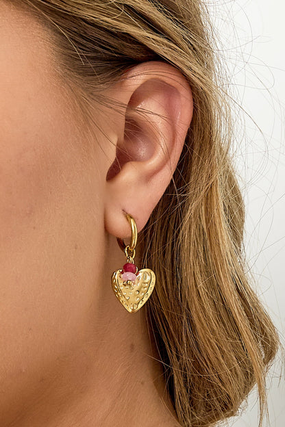 Side view close-up of woman’s ear showcasing single textured gold heart drop earring with pink and red beads