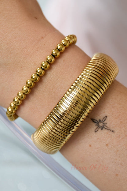 Model's wrist wearing a gold stretch bracelet paired with a shiny round-beaded gold bracelet, soft natural light