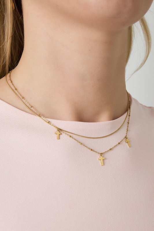Close-up of a woman wearing the gold layered cross charm necklace over a light pink top