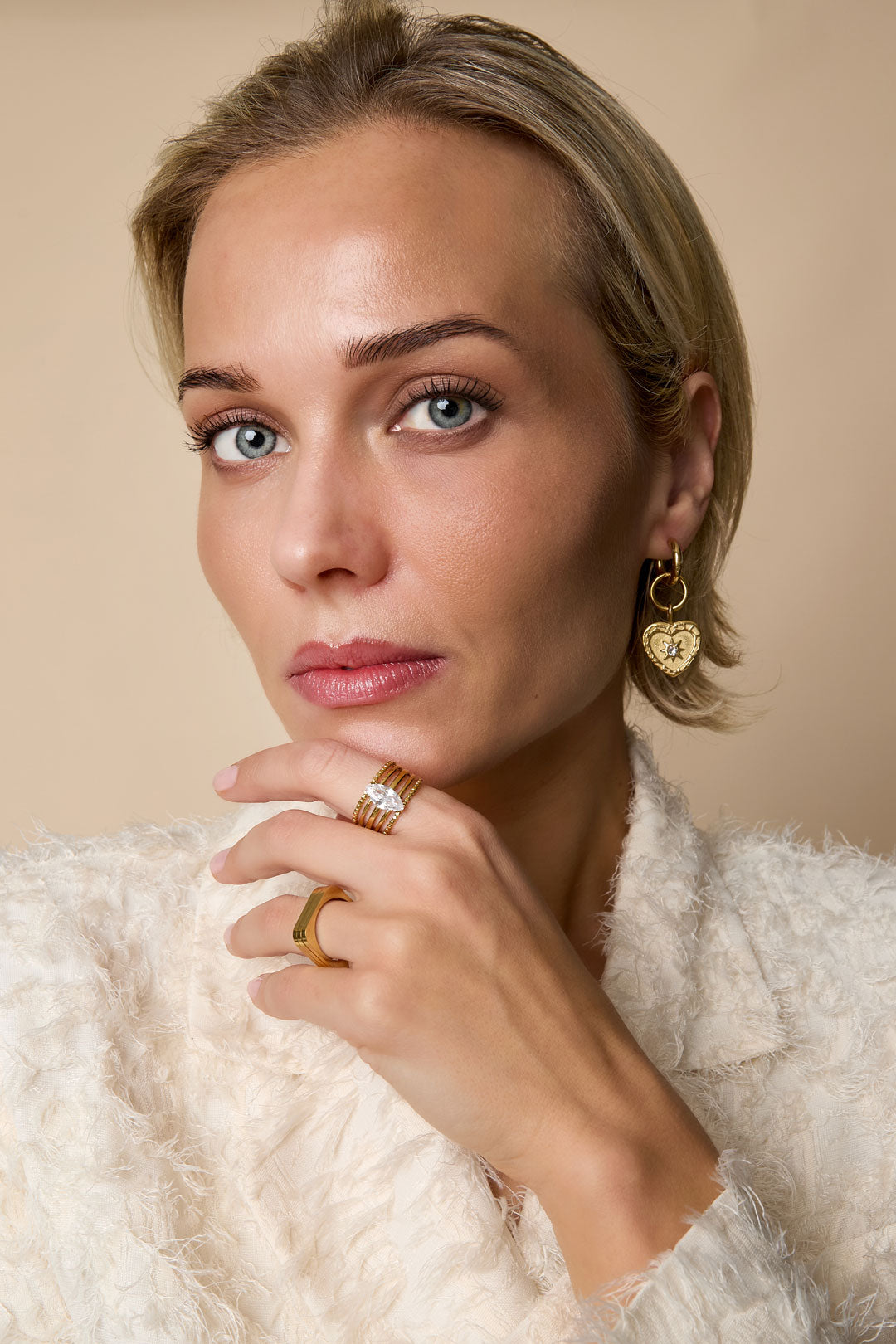 Woman wearing adjustable gold ring with marquise crystal gemstone and minimalist gold band, paired with matching gold heart-shaped earrings