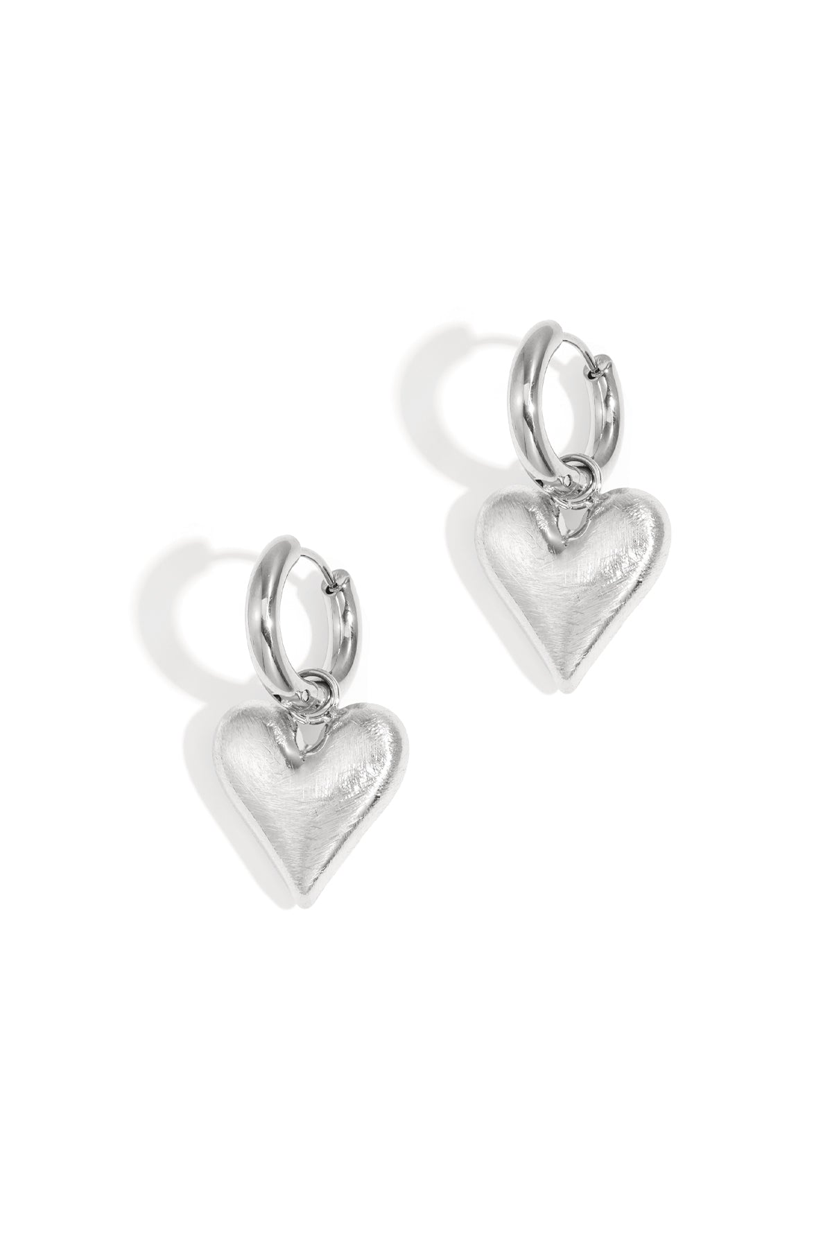 Pair of silver hoop earrings with dangling heart-shaped charms on white background