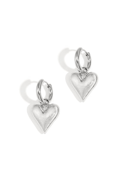 Pair of silver hoop earrings with dangling heart-shaped charms on white background