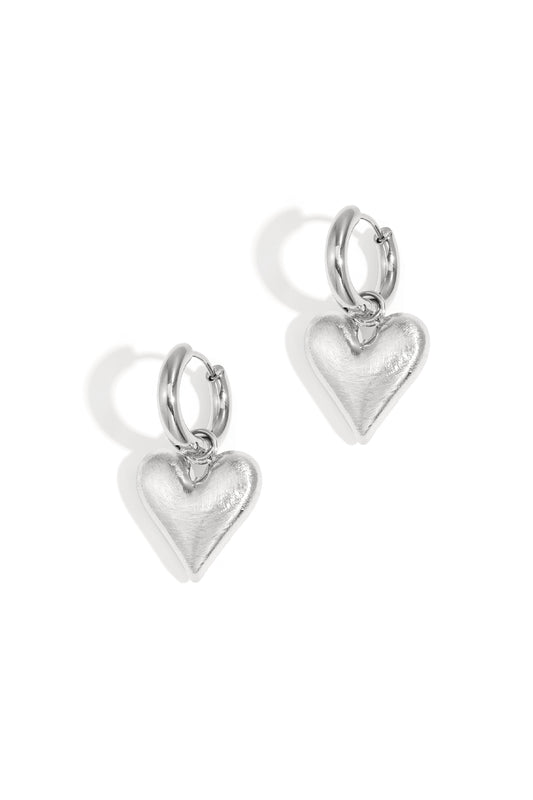 Pair of silver hoop earrings with dangling heart-shaped charms on white background