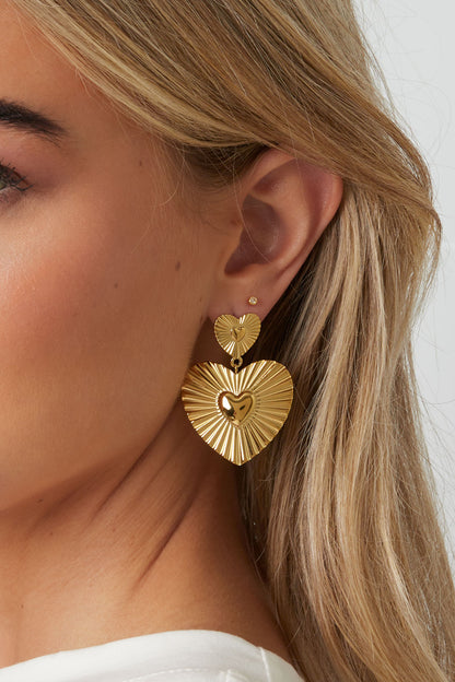 Detailed close-up view of gold heart drop earring worn by model showing grooved texture and polished center heart