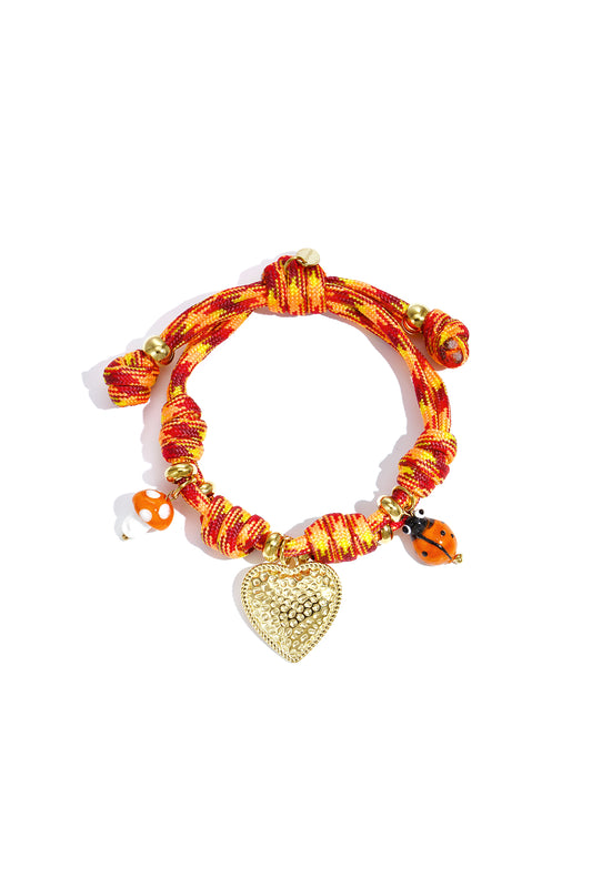 Colorful orange-red knotted rope charm bracelet with a gold textured heart pendant, mushroom and ladybug charms.