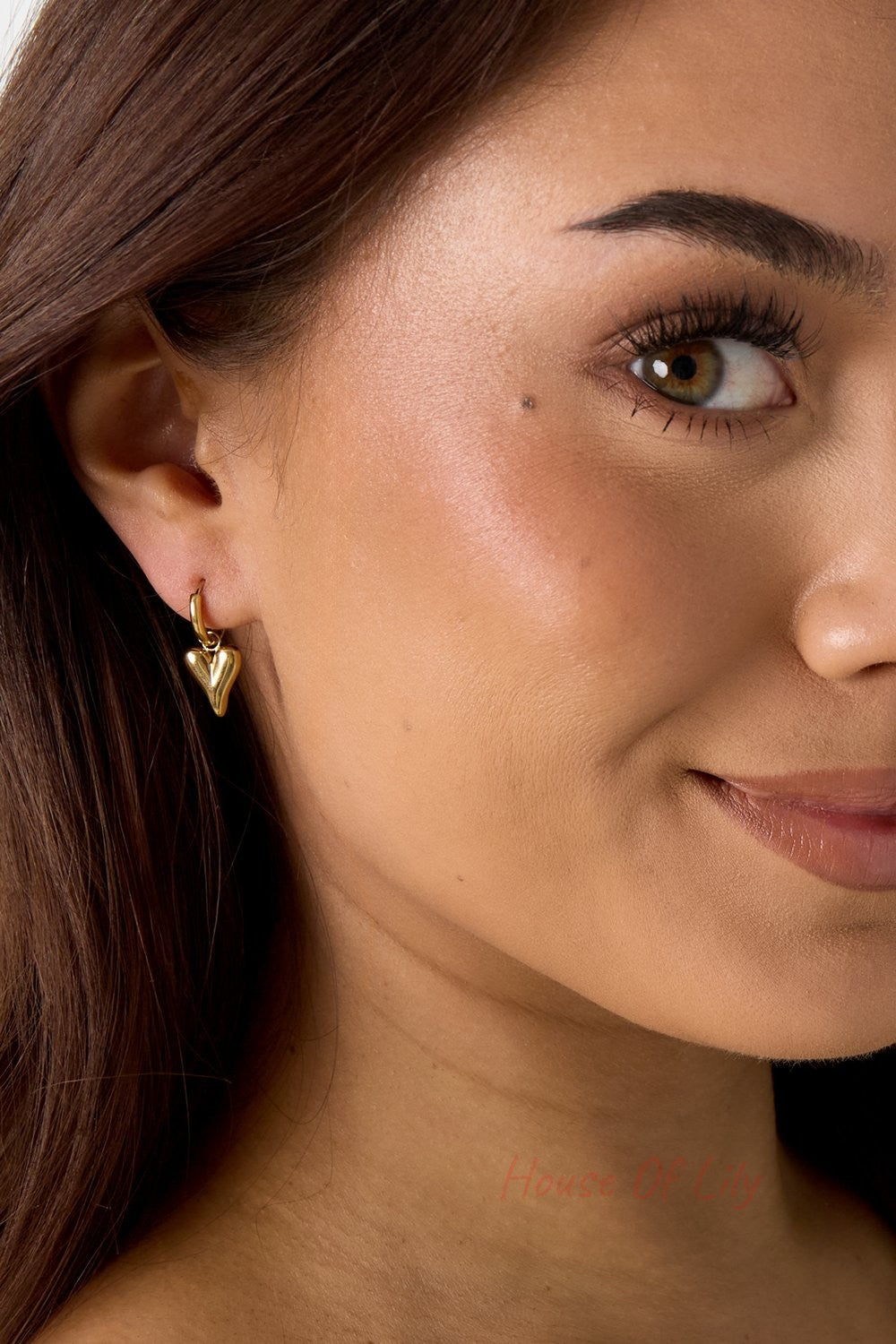 Main Character Heart Drops: Small, polished gold hoop earrings featuring a dainty, puffed heart charm on a woman’s ear.