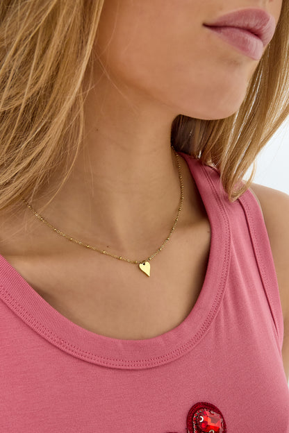 Close-up side view of the gold heart pendant necklace worn by woman in a pink top, showcasing the necklace’s delicate beaded chain.
